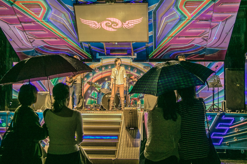 Red Roomers watch an outside performance under umbrellas.